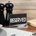 A table with a Cal-Mil Classic Acrylic Displayette holding a reserved sign and salt and pepper shakers.