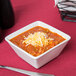 A Tuxton TuxTrendz bright white square china bowl filled with chili and cheese with a spoon.