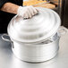 A person wearing gloves holding a Town aluminum steamer cover over a pot.