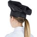 A woman wearing a black Chef Revival chef hat with adjustable head band.