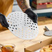 A round, perforated metal pizza disk being held above a wooden surface.