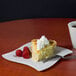 A piece of pie with whipped cream and raspberries on a Fineline white plastic square plate.