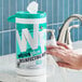 A container of WipesPlus 8" x 7" lemon scent alcohol-free surface disinfecting wipes with a wipe being pulled out.