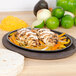 A Lodge oval wood underliner with a plate of chicken fajitas and vegetables on it.