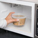 A hand holding a clear plastic tamper resistant deli container of food.