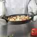 A person in a chef's uniform holding a Lodge mini cast iron oval casserole dish with food.