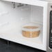 A 12 oz. clear plastic deli container with a tamper evident lid in a microwave.