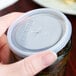 A hand places a Cambro translucent lid with a straw slot on a Cambro Laguna tumbler full of liquid.
