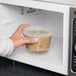 A hand holding a 16 oz. clear plastic deli container of food.