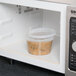 A clear plastic 16 oz. deli container of brown food in a microwave.