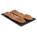 A pair of long loaves of bread on a black perforated baking tray.