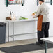 A person wearing an apron standing at a Regency stainless steel work table holding a bowl of vegetables.