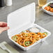 A white foam take out container with a perforated hinged lid, shown holding curly fries and a dipping sauce.