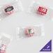 A group of small clear packages with pink and green logos containing different colored hard cinnamon balls.