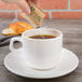 A hand pouring Regal Raw Turbinado Sugar from a small packet into a cup of coffee.