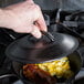 A hand holding a Lodge pre-seasoned cast iron lid over a pan of food.