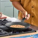 A pre-seasoned 10-inch carbon steel fry pan with a French-style handle being used to cook a pancake on a stovetop.