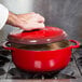 A person putting a lid on a Lodge Island Spice Red Enameled Cast Iron Dutch Oven.