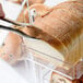 A person cutting a loaf of bread on a table using tongs.