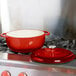 A Lodge Island Spice Red enameled cast iron Dutch oven on a stove.