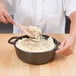 A person stirring food in a Lodge cast iron dutch oven with a wooden spoon.