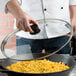 A person using a Lodge tempered glass cover to cook food in a cast iron skillet.