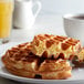 A plate of waffles with a pitcher of liquid next to a cup of coffee.