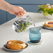 A hand pouring a glass pitcher of water with blueberries and mint leaves.