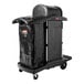 A black Rubbermaid janitor cart with a locking hood, cabinets, and an attached waste bag.