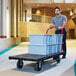A man pushing a Rubbermaid platform truck with boxes on it.