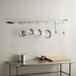 A kitchen with a Regency stainless steel wall mounted pot rack holding pots and pans.