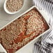 A loaf of bread with sunflower seeds in a white dish.