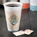 A 16 oz. Dart ThermoGlaze foam cup with a cafe espresso design, shown with sugar packets on a wooden surface.