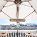A white Bromic Tungsten Smart-Heat electric patio heater under a table with a white umbrella.