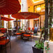 A Bromic Heating portable patio heater on an outdoor patio with tables and chairs under red umbrellas.