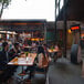 A group of people sitting at tables on an outdoor patio with a Bromic Heating Tungsten Smart-Heat Portable Propane Patio Heater on a table.