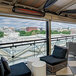 A black Bromic Tungsten Smart-Heat electric patio heater on a commercial patio with chairs and a black cushion.