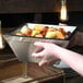 A person holding a square stainless steel bowl filled with fruit.