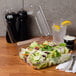 A salad in a Dart clear hinged plastic container on a table next to salt and pepper shakers and a glass of water.