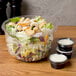 A salad in a Dart clear plastic bowl next to two small plastic cups of dipping sauces.