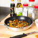A Carlisle aluminum non-stick fry pan full of vegetables and spices on a counter.