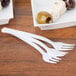 A square white container filled with Fineline white plastic tasting forks and olives.
