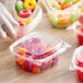 A hand holding a spoon over a Dart ClearPac plastic container of colorful candy.