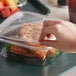 A close up of a hand holding a Dart deli container with food in it.