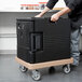 A man pushing a Cambro coffee beige Camdolly with a black container inside.