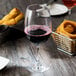 A close up of a Thunder Group plastic wine glass filled with red wine on a table with food.
