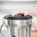 A person wearing plastic gloves opens a Waring stainless steel blender container.