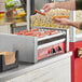 A man using an Avantco hot dog machine to prepare hot dogs.