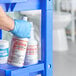 A hand in a blue glove holding a white plastic bottle of Noble Chemical Valient Ready-to-Use Disinfectant Toilet Bowl Cleaner.
