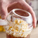 A hand holding a Dart clear plastic cup with whipped cream and a dome lid with a hole.